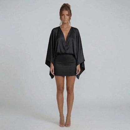Black cape-style mini dress with draped bodice and sleek skirt — styled view emphasizing dramatic structure.