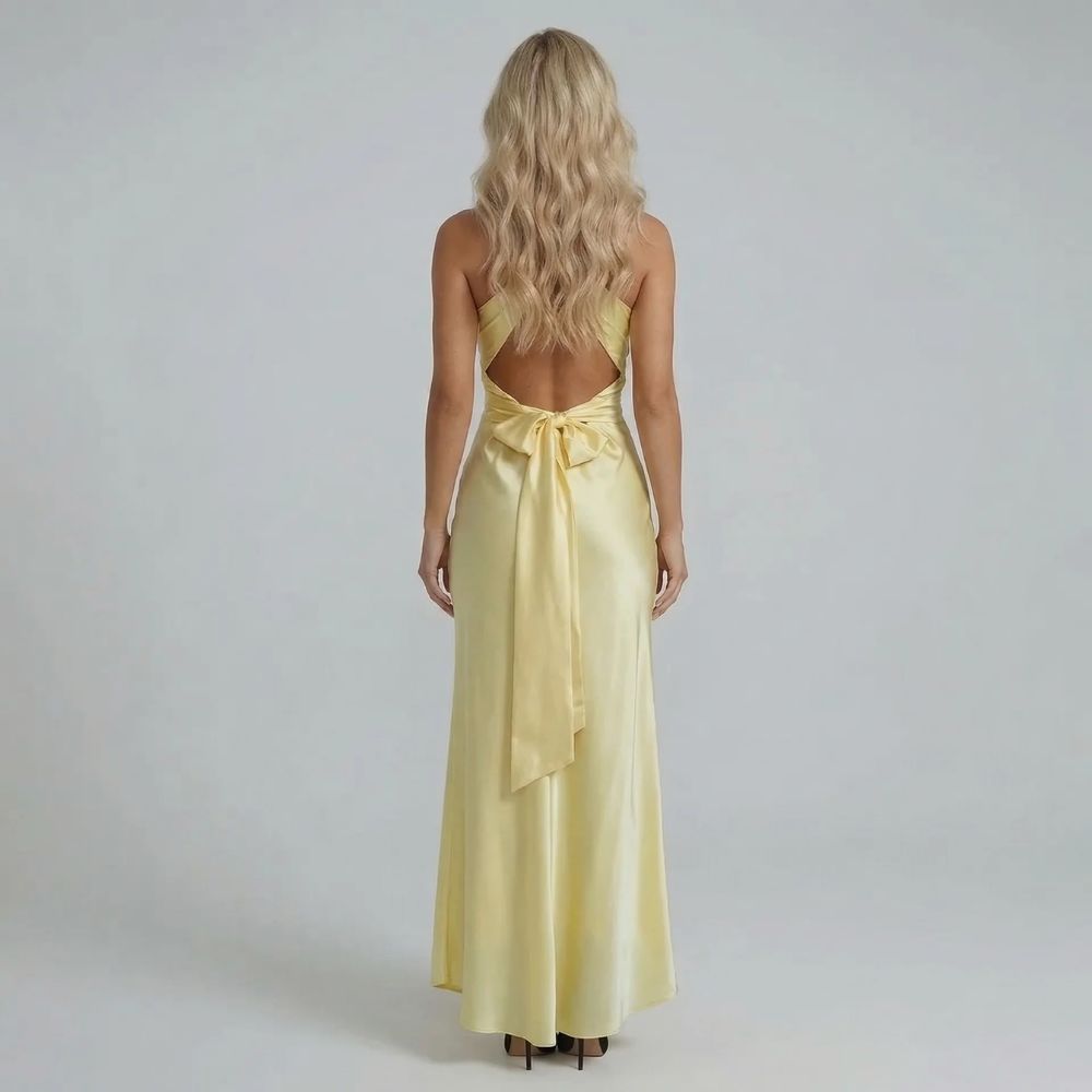 Yellow twist-bust maxi dress with bow-tied open back — rear view showing crisscross straps and oversized bow detail.
