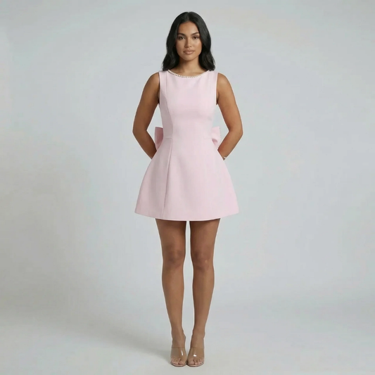 Pink fit-and-flare mini dress with pearl-trimmed neckline, oversized bow, and flared skirt — front view.